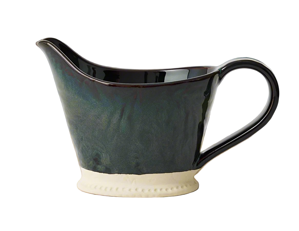 A stoneware pitcher with a figaure-like handle and a glazed finish in a combination of green and black colors.