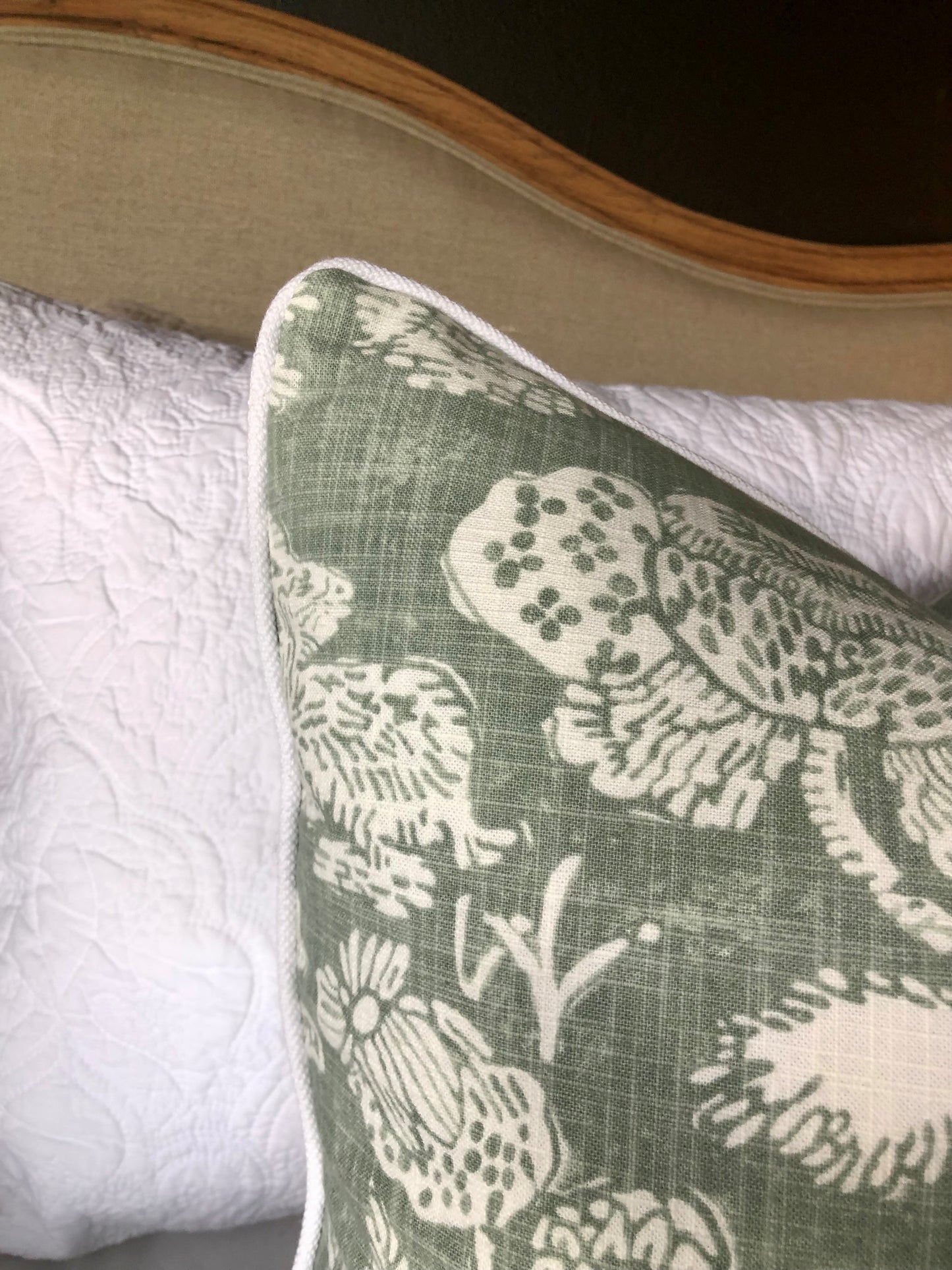 This elegant Richloom Platinum Howland Linen Moss Green Cushion is crafted from Richloom's global fabric house, featuring a graceful white pattern of trees and birds on a pale green background. Its sumptuous heavyweight fabric and the luxurious feather insert make it a perfect accent for your plush home decor. Corner close up.