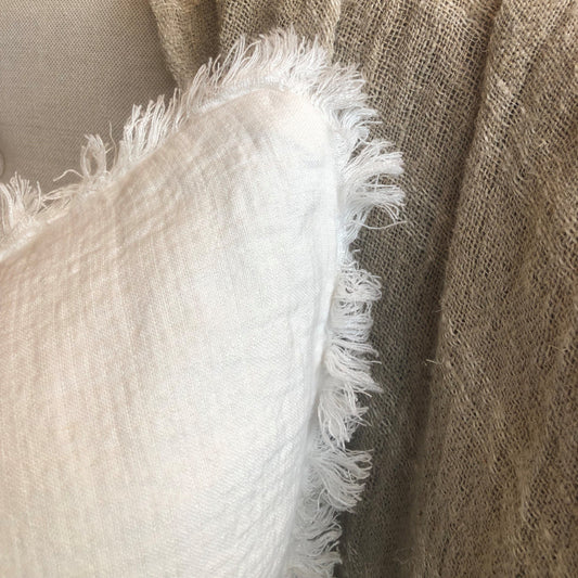 The Anais Pure French Linen Fringed Edge Cushion boasts a custom-woven fabric. It is feather filled for a luxuriously comfortable experience and finished with a charming, rustic egg shell white hue. Close up corner.