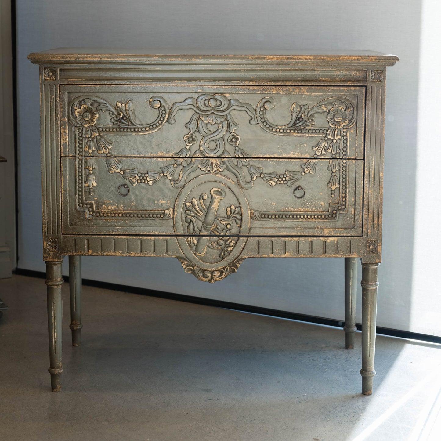 The unique and stunning one of a kind Daphne Sideboard boasts intricate carvings and distressed pale olive/grey painted finish. Crafted from mahogany and featuring two drawers, this versatile piece is perfect for a living or dining room in even in a bedroom. Front