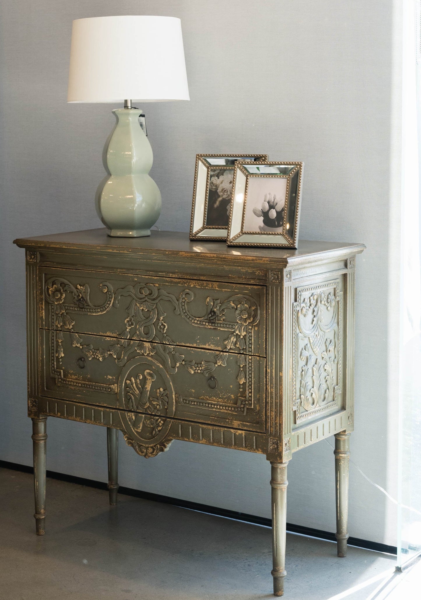 The unique and stunning one of a kind Daphne Sideboard boasts intricate carvings and distressed pale olive/grey painted finish. Crafted from mahogany and featuring two drawers, this versatile piece is perfect for a living or dining room in even in a bedroom. Front