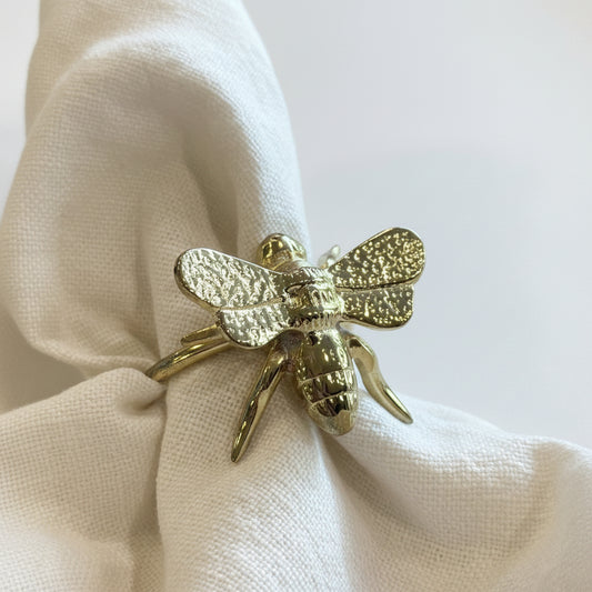 Gold bee-shaped ring on a white fabric background
