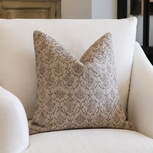 A white slipcovered armchair in a styled living room setting, featuring a textured beige and gray patterned accent pillow.