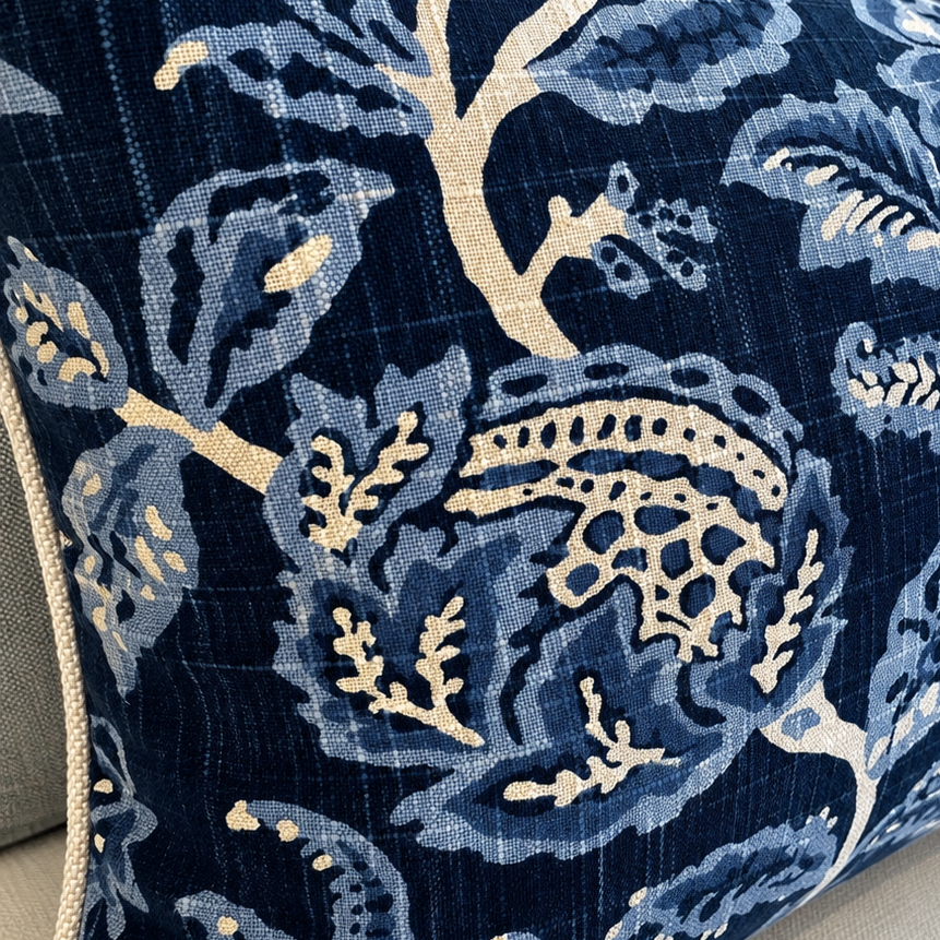 A close-up of a decorative throw pillow featuring a navy blue and light blue floral pattern with cream accents, resting on a light beige sofa.