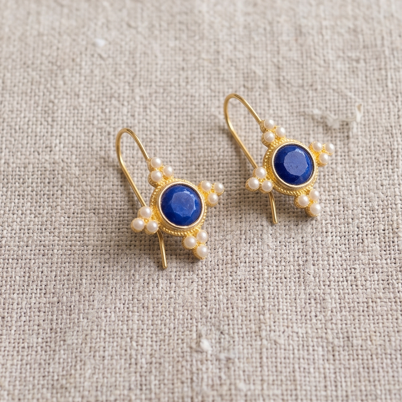 Gold earrings with blue stones on a beige fabric background