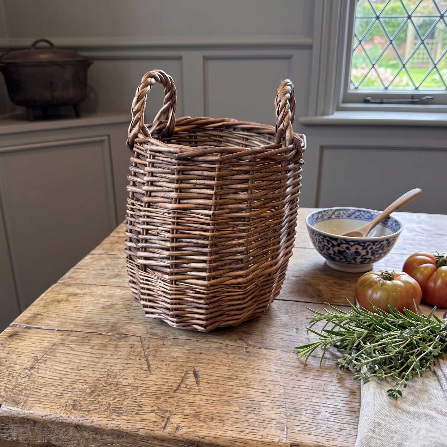 Wicker basket on a wooden table with tomatoes and herbs near a window.