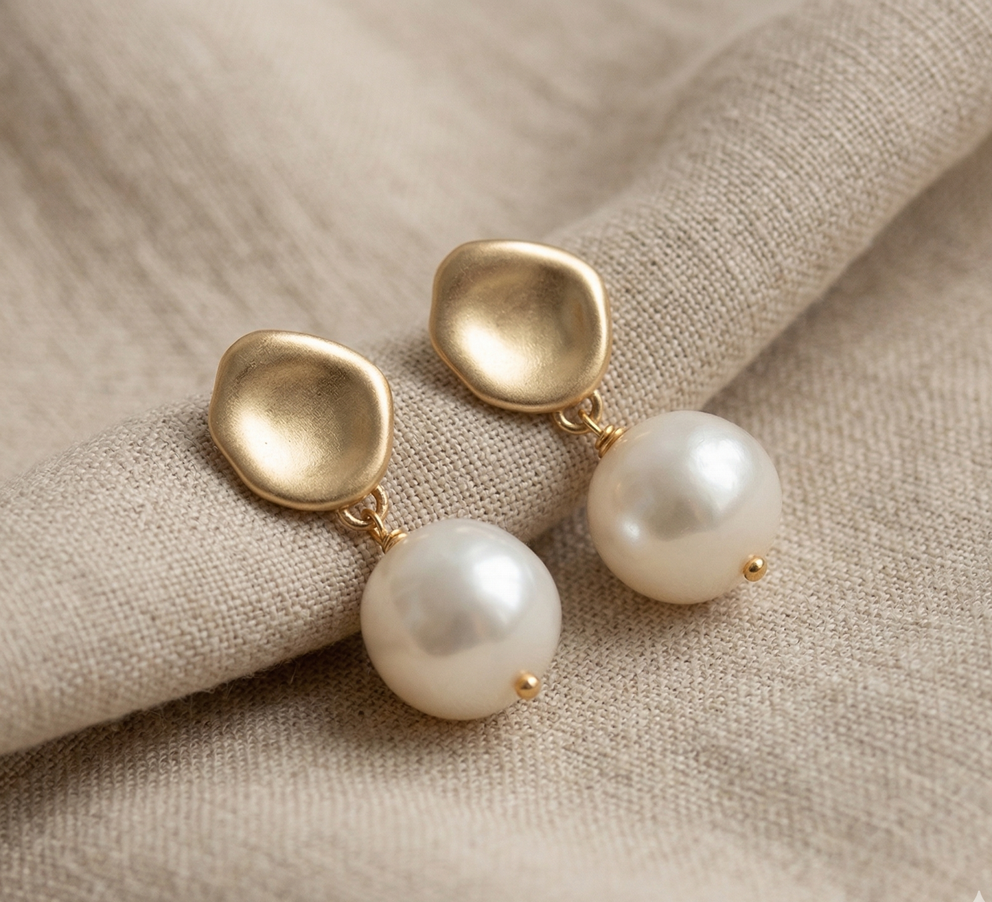 Gold earrings with pearls on a beige fabric background
