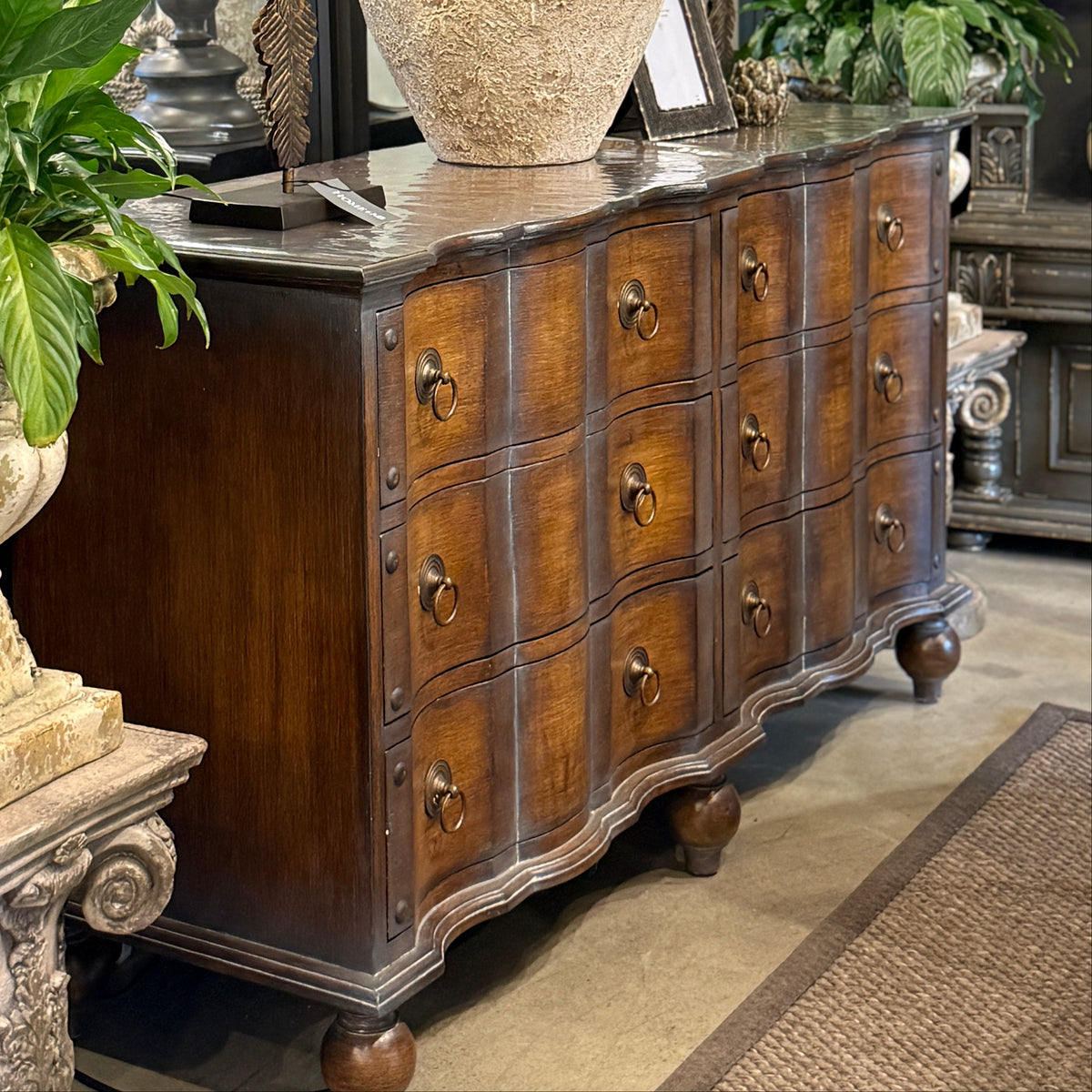 Wooden dresser with decorative items including a lamp, vase, and plants in a store setting.