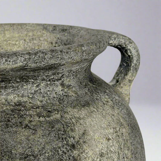 Close-up of a textured stone pot with a handle on a light gray background