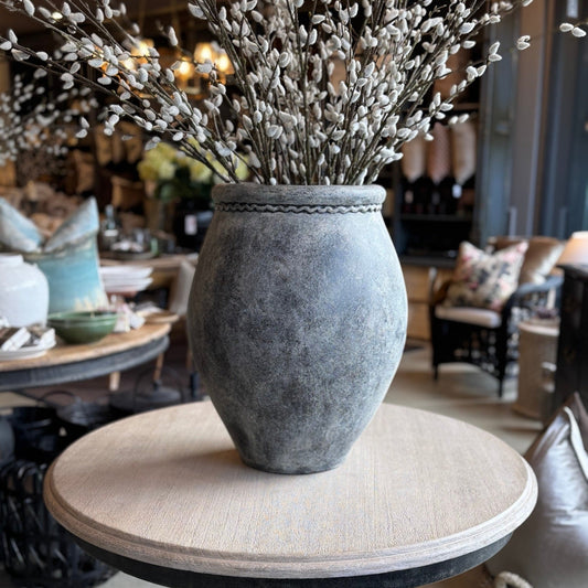 Decorative vase with willow branches on a round table in a room setting.