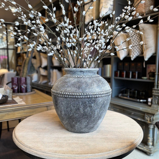 Decorative vase with willow branches on a round wooden table in a store setting
