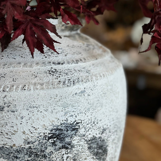 Decorative vase with textured surface and red leaves on a blurred background