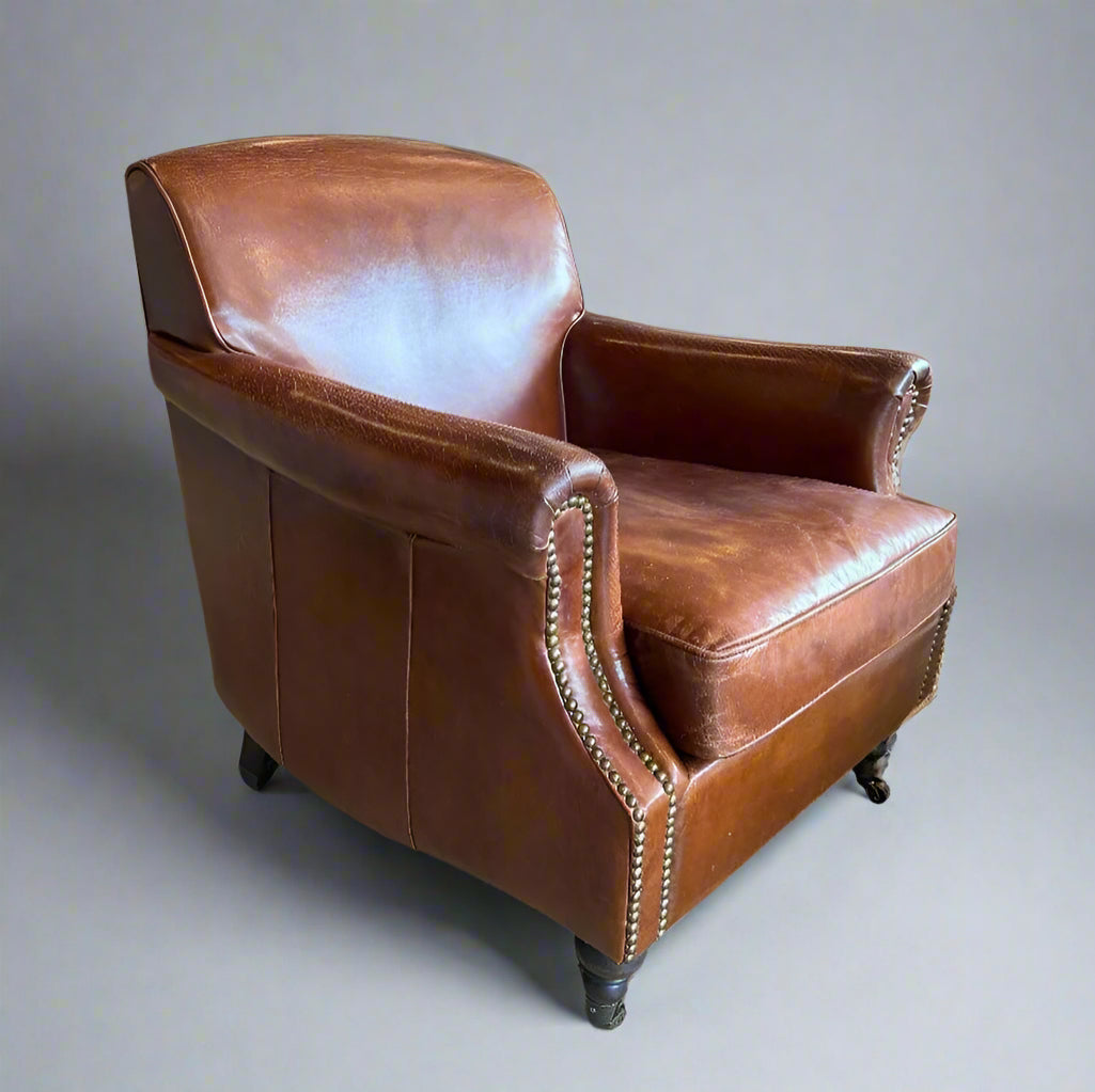 The Oliver Aged Leather Armchair boasts top grain cowhide upholstery, expertly aged by hand for a timeless and vintage appearance. Finished with charming brass stud accents and castor wheel feet. Side