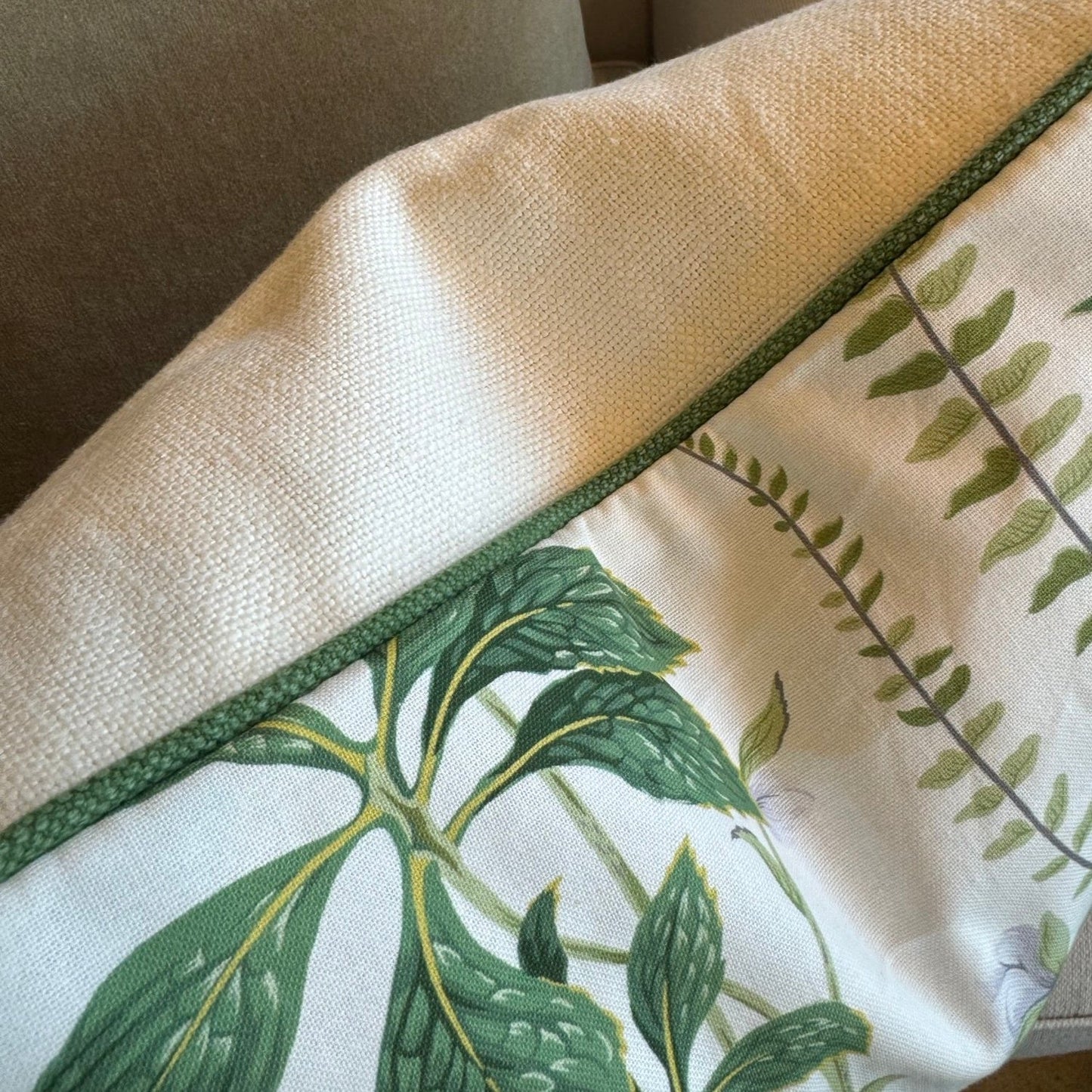 The uniquely beautiful Marguerite Camelia Floral Cushion showcases a stunning floral pattern in soft white and green against a warm ivory backdrop. The self piping in dark green adds a touch of sophistication, while the feather insert ensures unparalleled comfort. For a flawless finish, the reverse side is also lined with a contrasting ivory solid.