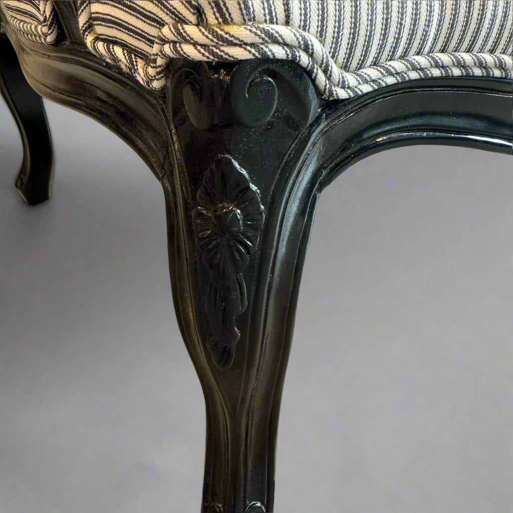 Indulge in timeless French style with this elegant armchair, exquisitely crafted from sturdy mahogany and finished with a sleek black gloss. Its luxurious hand-carved details and sturdy frame add a touch of sophistication to any living room or bedroom, while the stunning blue and white ticking fabric upholstery adds a subtle yet eye-catching touch. Elevate your space with this expertly crafted piece that exudes elegance and charm.