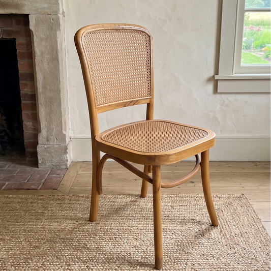 Wooden chair with wicker back and seat in a room with a fireplace and window.