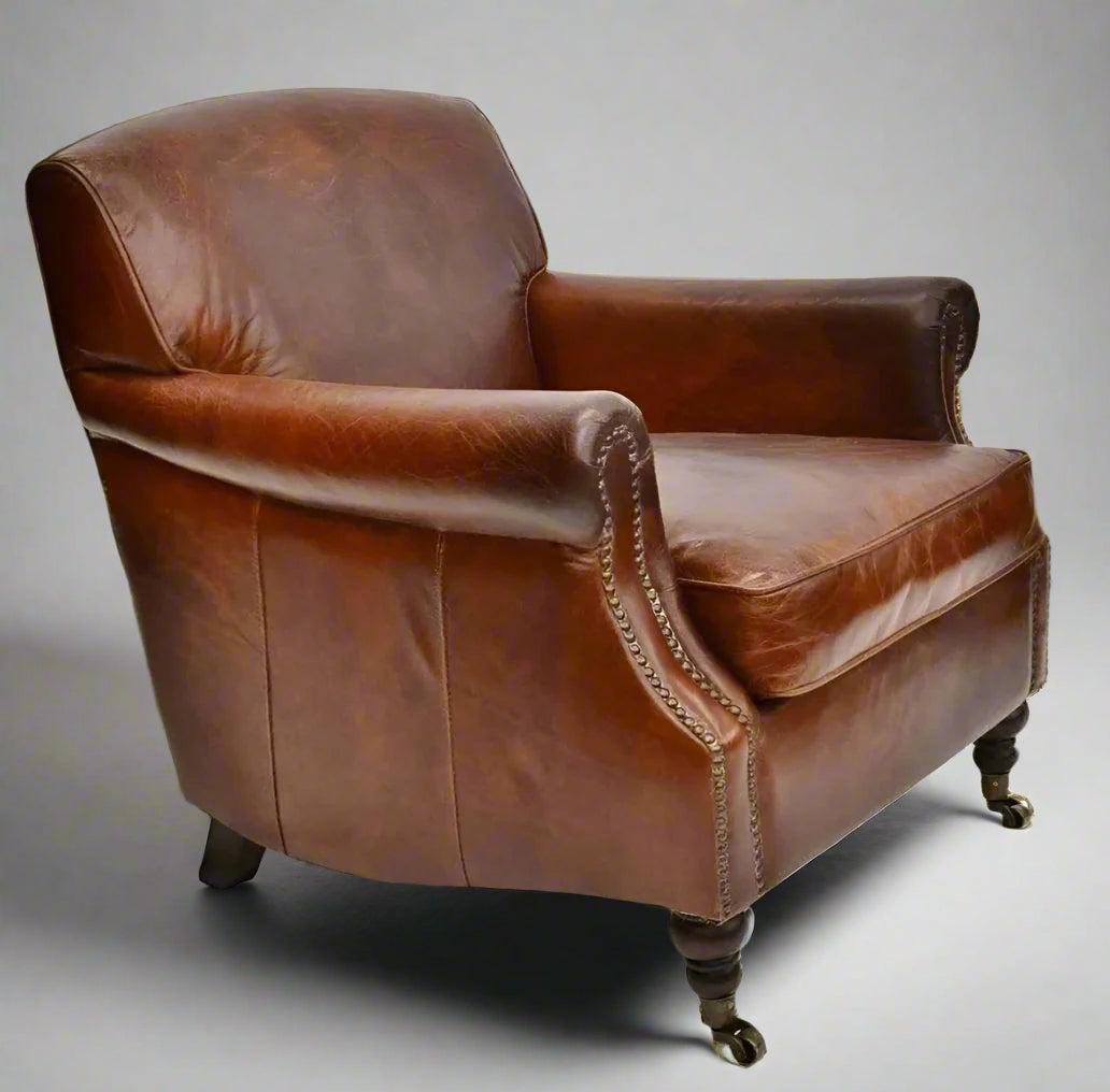 The Oliver Aged Leather Armchair boasts top grain cowhide upholstery, expertly aged by hand for a timeless and vintage appearance. Finished with charming brass stud accents and castor wheel feet. Side