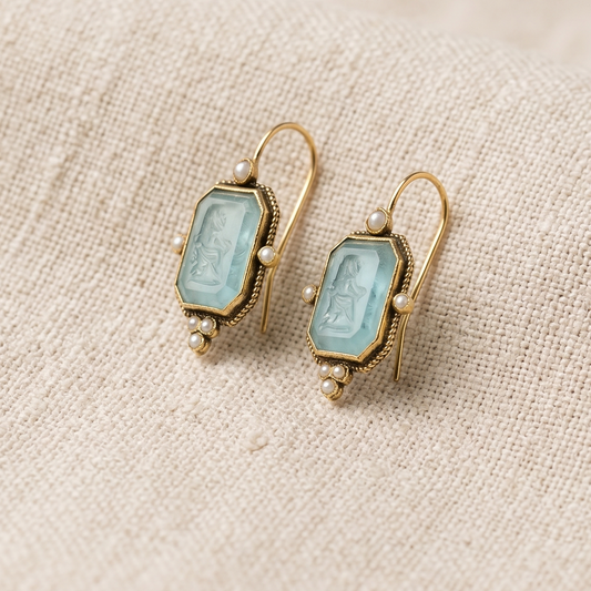 Pair of gold earrings with light blue gemstones on a beige fabric background