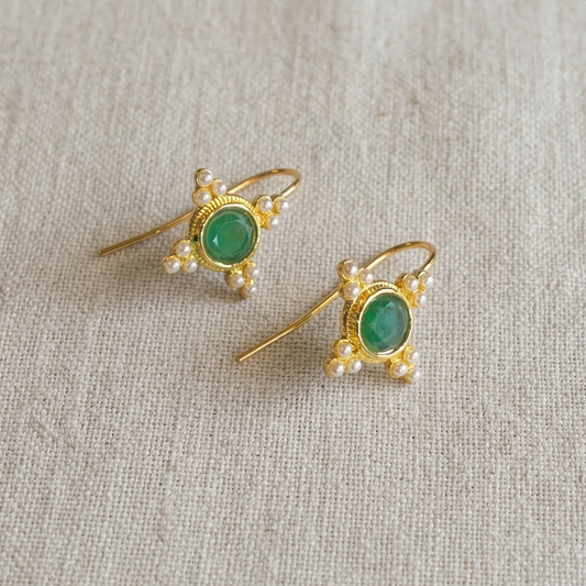 Pair of gold earrings with green gemstones on a light fabric background