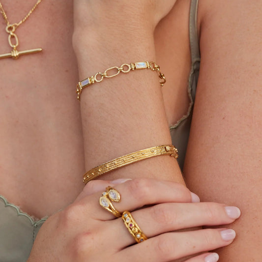 Close-up of a person's wrist and hand wearing gold jewelry including bracelets and rings.