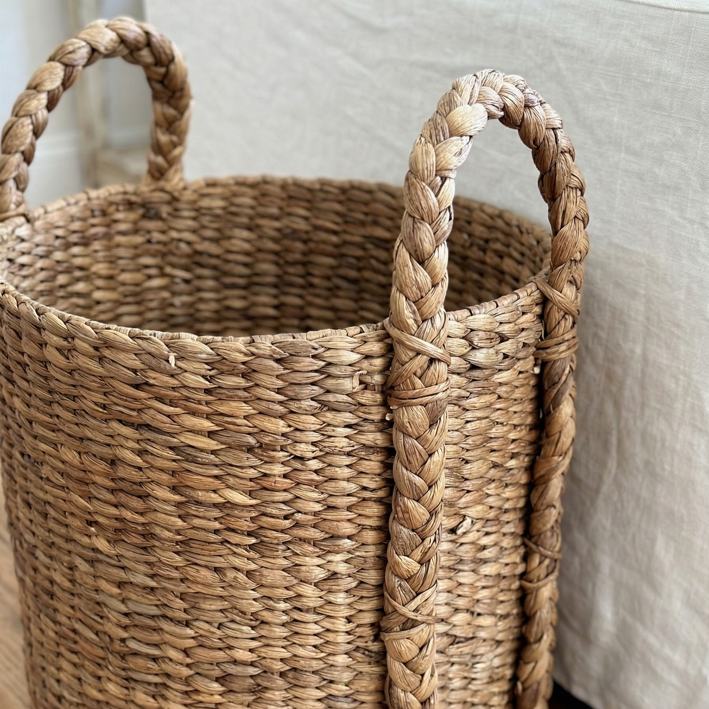 Woven basket with handles on a wooden floor next to a bed