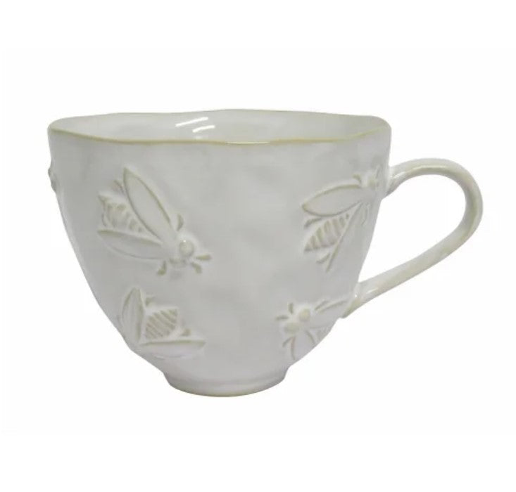 White ceramic mug with bee embossing on a wooden table with a teapot and lavender.