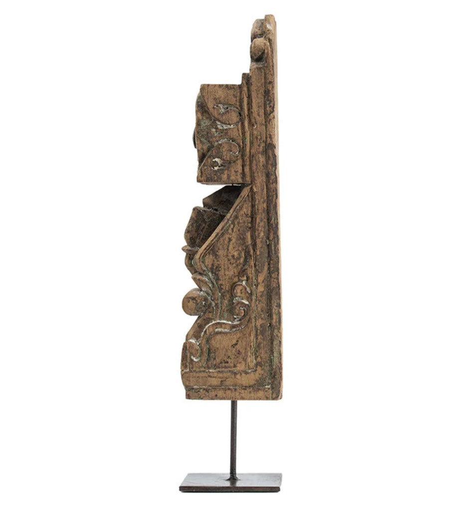 Add a touch of culture to your living room with this stunning Gujrati Toda Wood Sculpture On Metal Stand. Made with distressed wood and featuring intricate carving, it sits on a sturdy metal stand and exudes a rustic charm. Its weathered grey finish and square base give it the appearance of a museum piece, making it a perfect addition to coffee tables, bookshelves, and more.