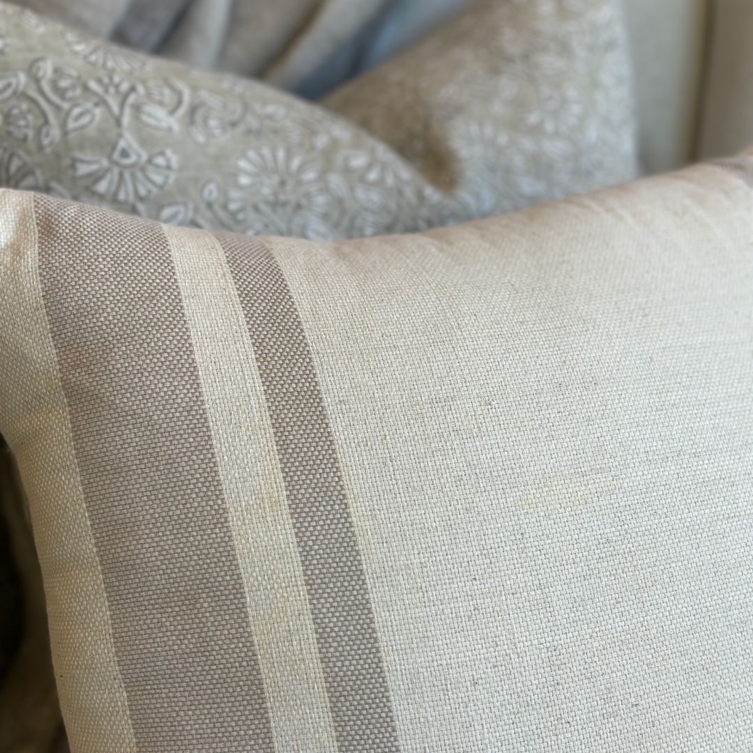 The Jambi Handwoven Cotton Beige Cushion is made from high-quality cotton, giving it a natural texture. Adorned with beautiful taupe stripes, it effortlessly complements any room and style with its muted beige tones. Styled detail.