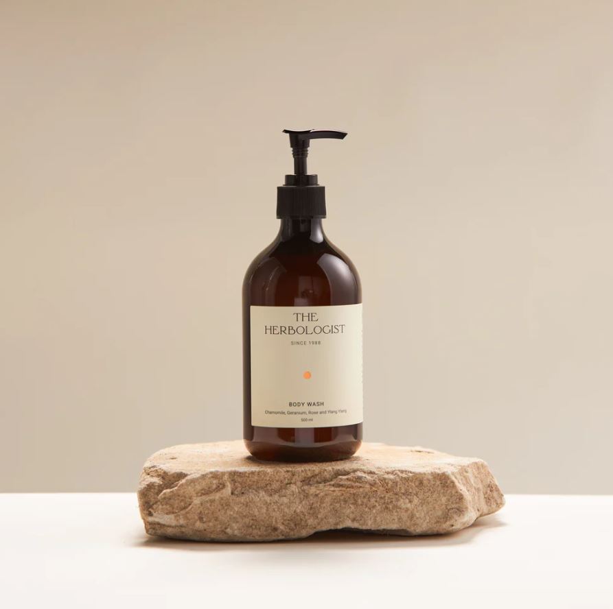 Brown bottle with pump labeled 'The Herbologist' on a stone surface against a beige background