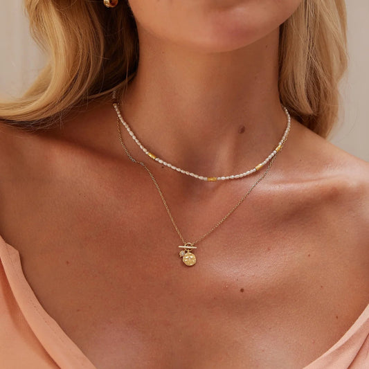 Close-up of a woman wearing a gold necklace with a pendant against a neutral background