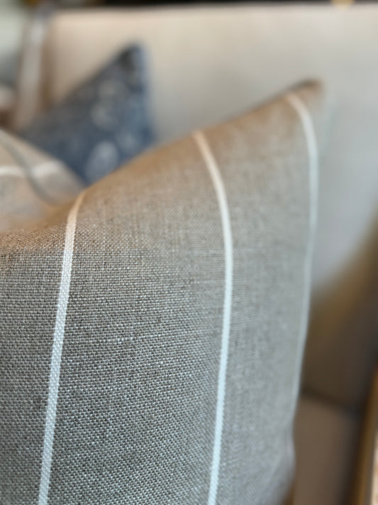Indulgently fashioned from a luxurious, durable fabric, this exquisite Wortley Narrow Neutral White Stripe Cushion boasts a classic white stripe on a warm neutral background. It's the perfect timeless and graceful accent to elevate any home decor. Includes a luxurious feather insert. Close up corner.