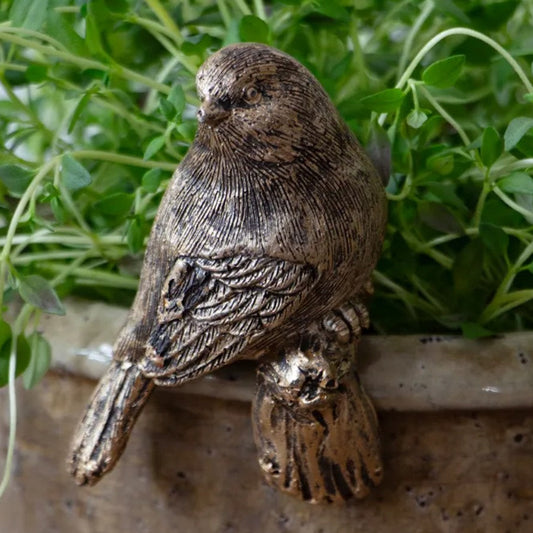 Bronze bird figurine on a stone surface with green plants in the background