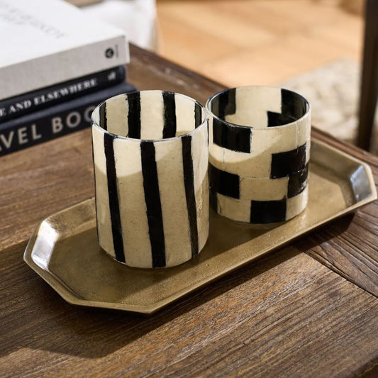 Two black and white patterned cups on a gold tray with books in the background.
