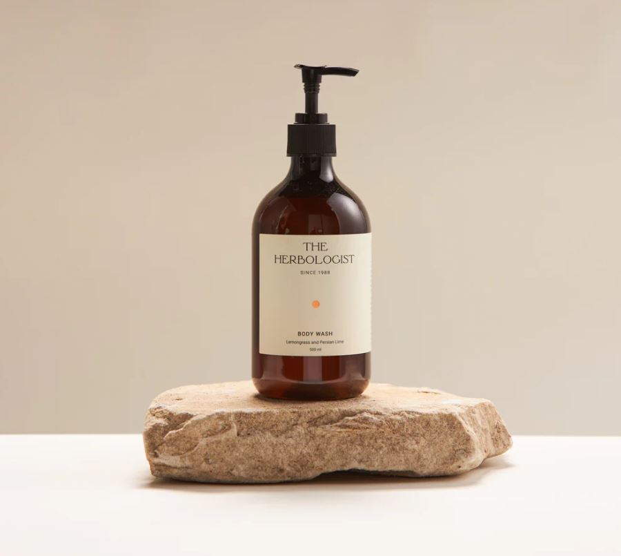 Bottle of 'The Herbologist' body wash on a stone surface with a beige background