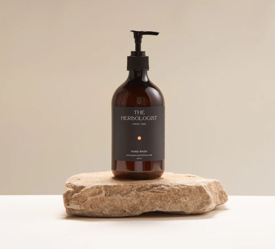 Bottle of 'The Herbolologist' hand wash on a stone surface with a beige background
