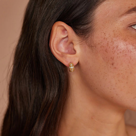 Close-up of a person wearing a gold earring with a neutral background