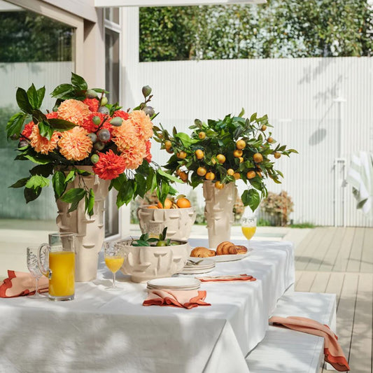 Outdoor table setting with floral arrangements and breakfast items on a sunny day.
