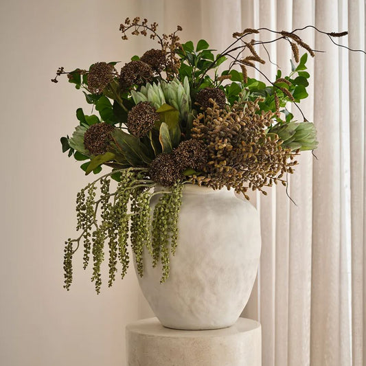White vase with a bouquet of green and brown flowers on a neutral background