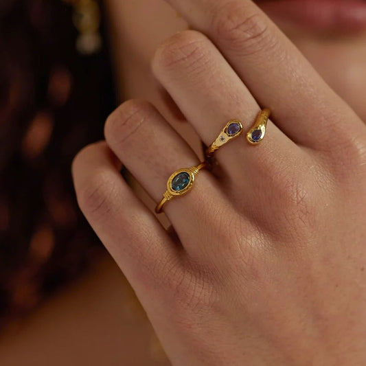 Close-up of a hand wearing gold rings with yellow flowers held near the face.