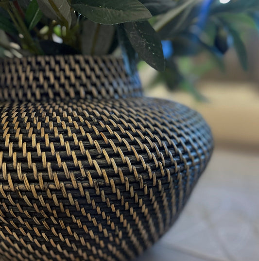 Let the Raja Rattan Vase enchant you with its stunning craftsmanship and tight weave that emanates a calming and natural vibe. This exquisite piece will bring character and coziness to your living space, and its adaptable design allows for beautiful floral arrangements or a simple, raw look. With a captivating blend of black and neutral tones, this vase is truly a must-have for any home. Close up.