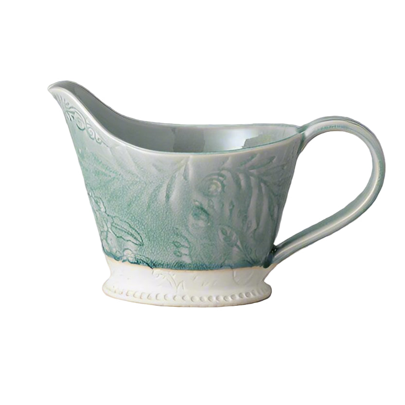 A green and white arabesque-patterned ceramic pitcher with a handle.