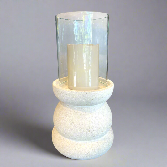 The Handcrafted Whitestone Candle Holder is expertly made from prime whitestone, complete with a recycled glass cylinder lantern. Its elegant curves complement the tall pillar candles that grace its one-of-a-kind design, creating a beautiful display. Front.