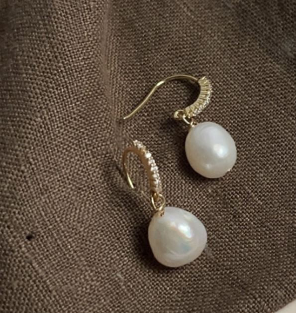 Pearl earrings with gold hooks on a brown textured fabric background