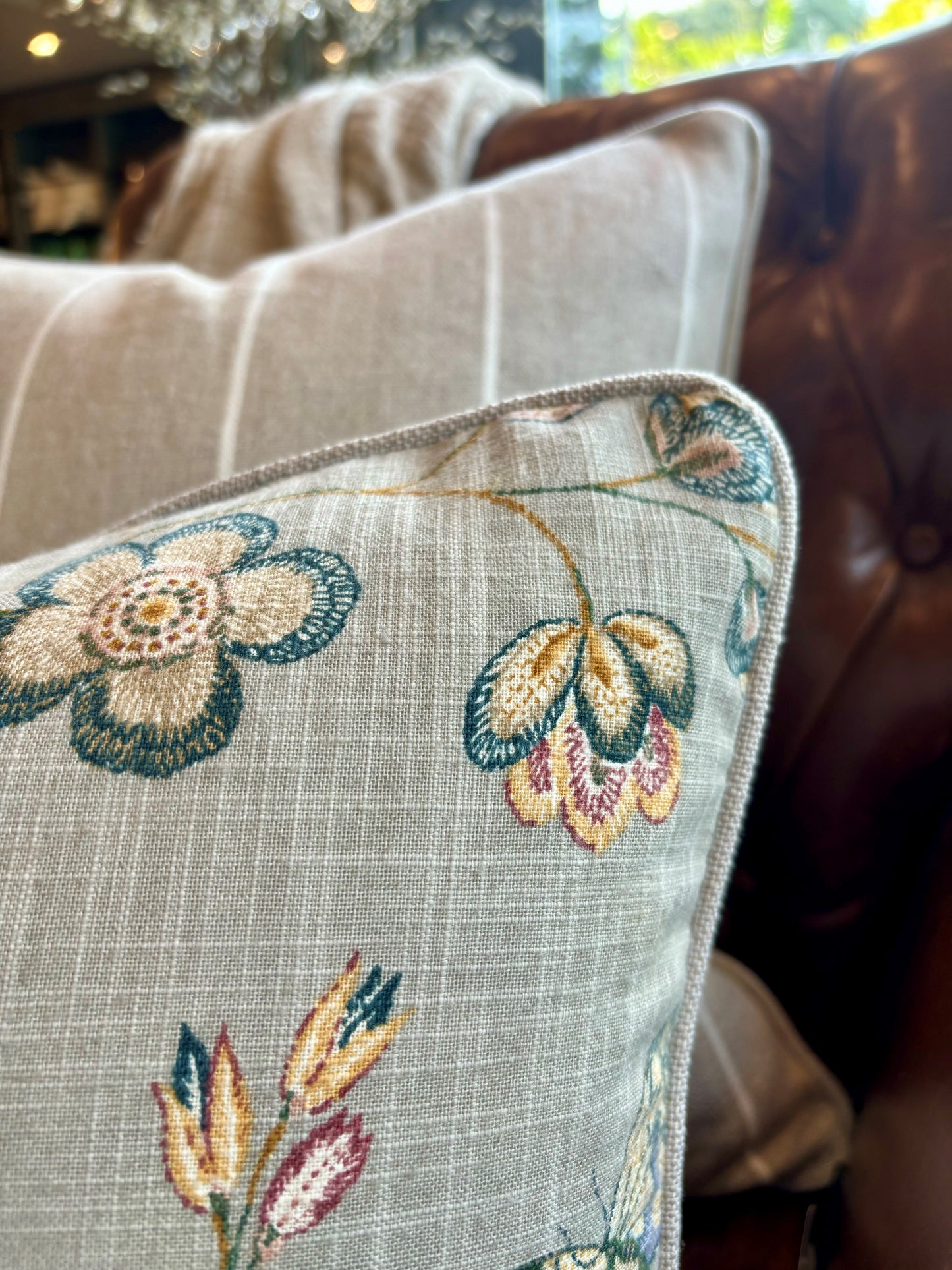 Indulge in the exquisite artistry of the Claudette Floral Linen Lumbar Cushion. Crafted from a sturdy linen blend, it showcases a stunning floral pattern in vibrant hues against a subtle taupe background, with a reverse side of elegant neutral fabric. A feather insert adds an extra touch of comfort. Corner close up.