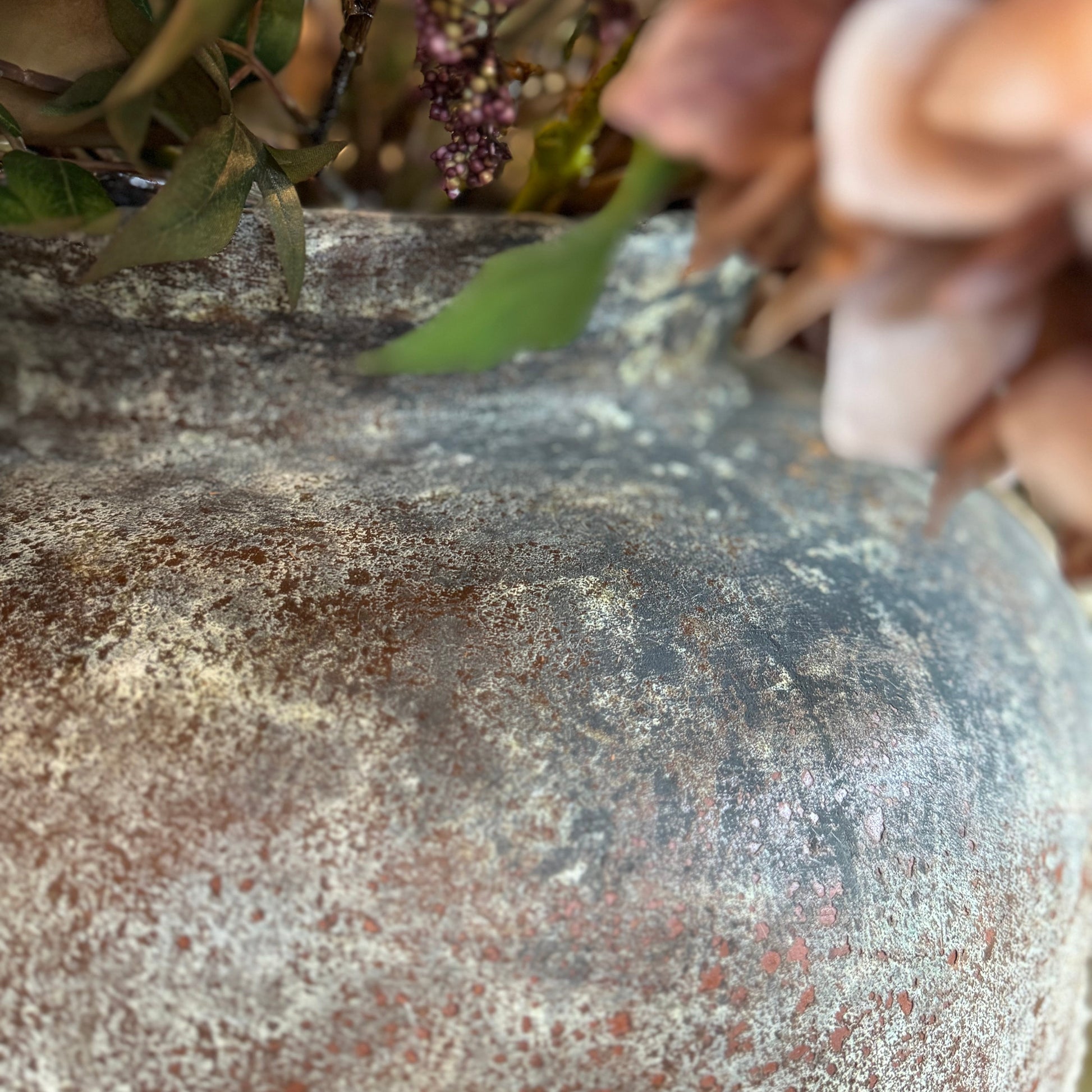 Close-up of a textured stone vase with flowers and greenery.