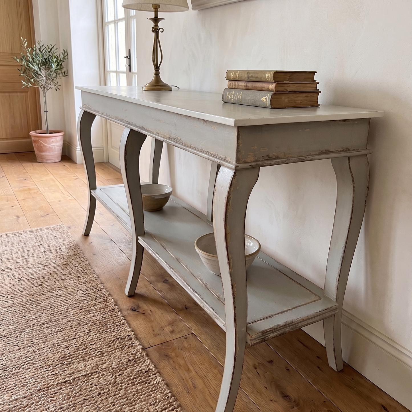Console table with books and a lamp in a room with wooden flooring and a mirror on the wall.