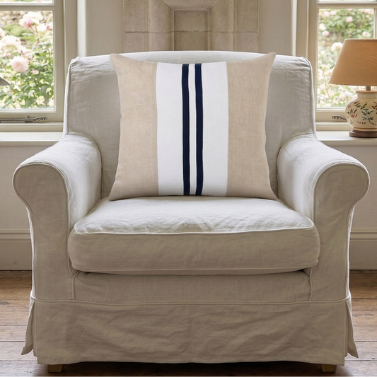 Beige armchair with a striped pillow in a room with large windows and a fireplace.