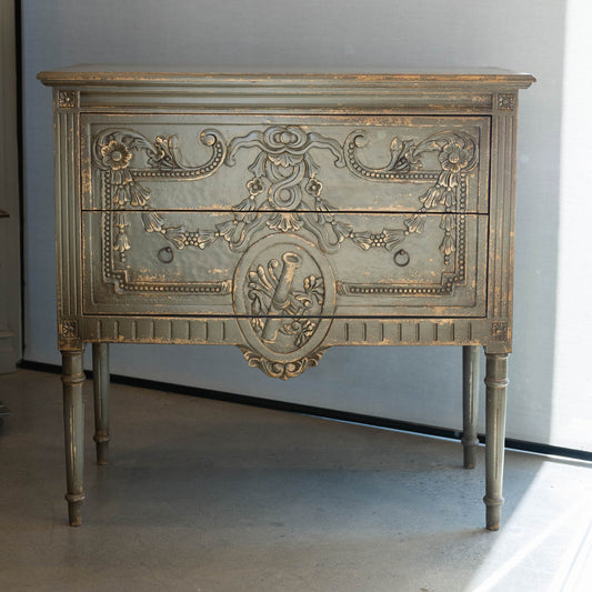 The unique and stunning one of a kind Daphne Sideboard boasts intricate carvings and distressed pale olive/grey painted finish. Crafted from mahogany and featuring two drawers, this versatile piece is perfect for a living or dining room in even in a bedroom. Front