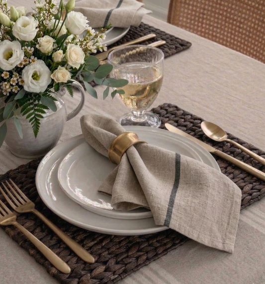 Elegant table setting with white flowers, gold cutlery, and a vase on a woven placemat.