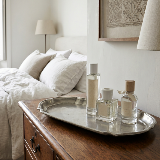 Tray with perfume bottles on a wooden dresser next to a bed in a bedroom.
